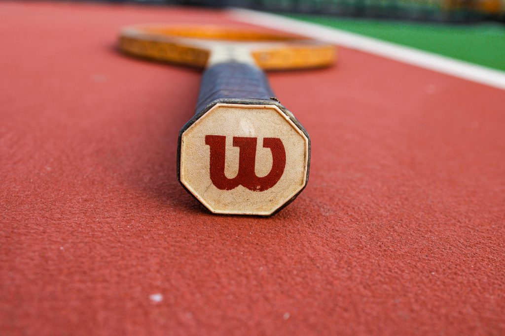 Detailed close-up of a tennis racket on a vibrant red tennis court surface.