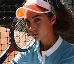 Close-up of a young female tennis player with racket on clay court.